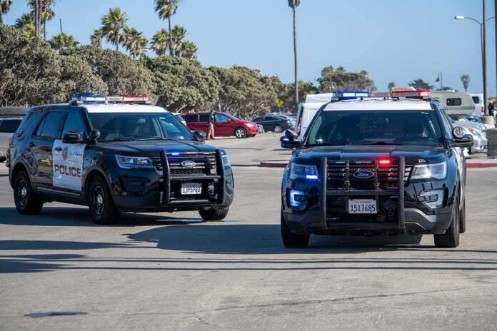 Two police SUVs with lights on in a coastal parking lot