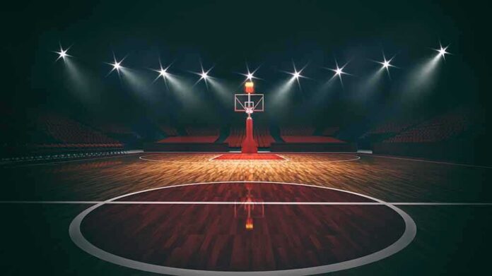 shutterstock_1933345100-2 Basketball hoop on an empty indoor court under bright arena lights