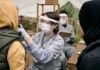 Healthcare worker in protective gear examines a patient at an outdoor clinic