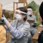Healthcare worker in protective gear examines a patient at an outdoor clinic