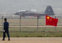 Nuclear-Capable MiGs Vanish—Iran Blocked Stealth fighter jet on runway behind fence with Chinese flag in foreground