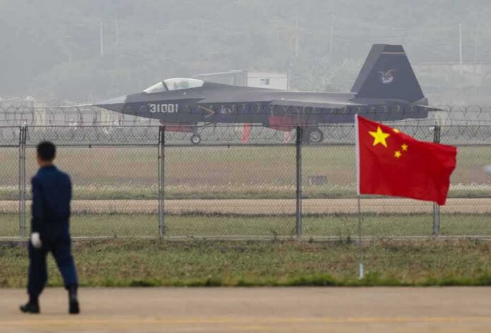Stealth fighter jet on runway behind fence with Chinese flag in foreground