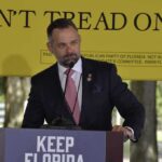 Spending Bloodbath Looms In Florida man in suit speaking at a podium outdoors