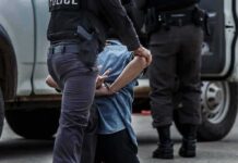 Earpiece Intruder Rattles Trump Course Police officer detaining a handcuffed person beside a vehicle