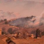 Wildfire burns on hillside near suburban homes