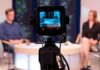 Camera focused on a television studio interview with two seated hosts