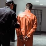 School Scandal Triggers Fast Removal Police officer escorting handcuffed inmate in orange jumpsuit