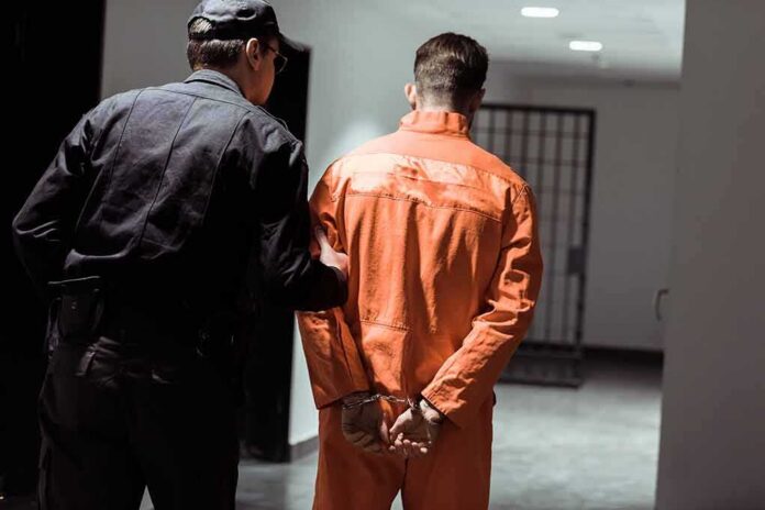 shutterstock_1030254055-7 Police officer escorting handcuffed inmate in orange jumpsuit