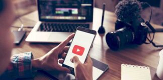Hands holding smartphone with video app icon at a workspace
