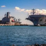 Aircraft carrier and support ships docked at a naval harbor