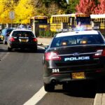 Police cars with flashing lights near school buses on a city street
