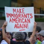 Austin ICE Shooting Turns Political Teddy Williams at a protest holding a sign reading 'Make Immigrants American Again'