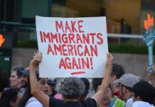 Austin ICE Shooting Turns Political Teddy Williams at a protest holding a sign reading 'Make Immigrants American Again'