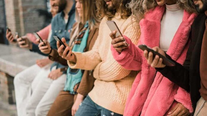 shutterstock_1688058088 group of people using smartphones while standing in a row