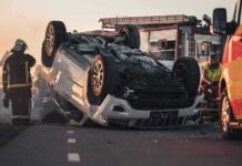 Overturned car on road with firefighters and ambulance