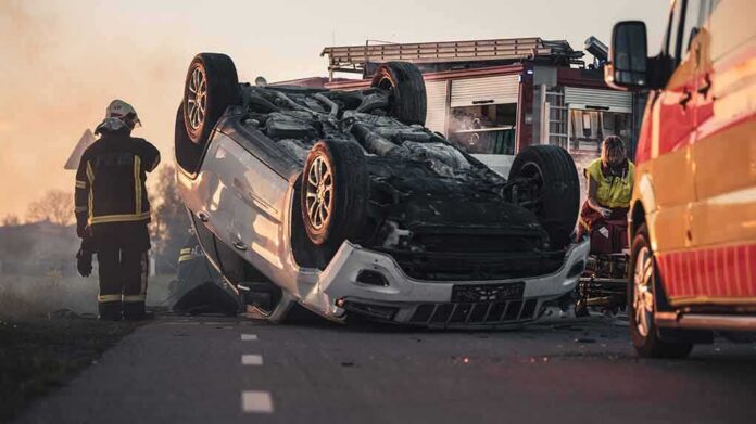 shutterstock_1721682409 Overturned car on road with firefighters and ambulance