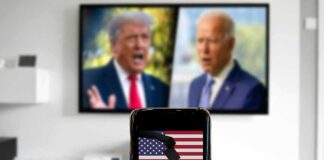 Smartphone with ballot icon held before a TV showing two blurred politicians