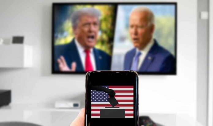 Smartphone with ballot icon held before a TV showing two blurred politicians