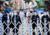 Police officers in masks and face shields stand behind a street barricade
