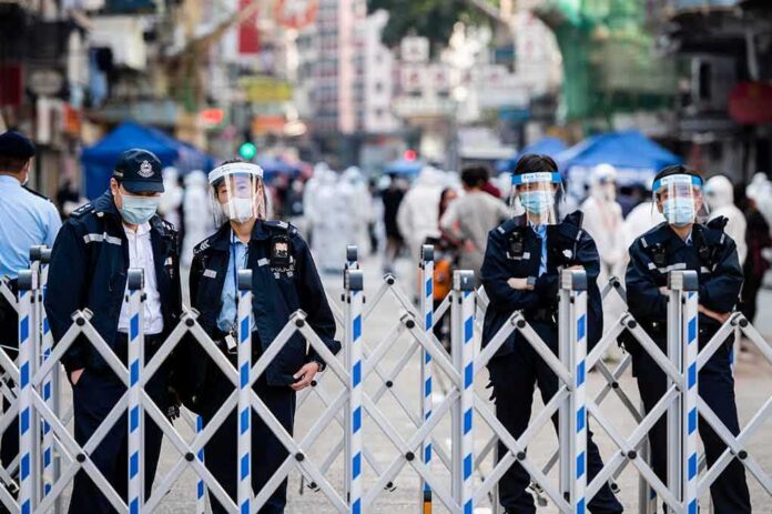 Police officers in masks and face shields stand behind a street barricade