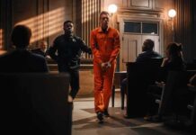 Inmate in orange jumpsuit escorted by officer in courtroom