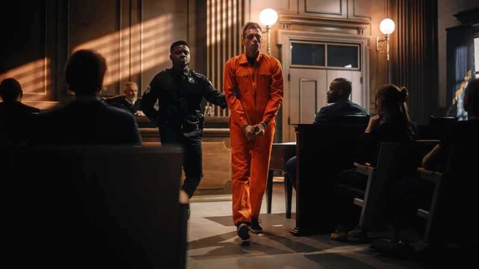 shutterstock_2056444856-8 Inmate in orange jumpsuit escorted by officer in courtroom
