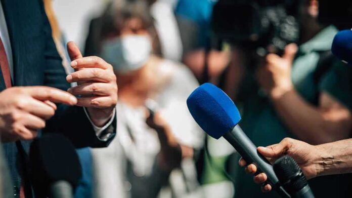 shutterstock_2166827699 Microphones held toward a speaker at an outdoor press event