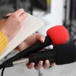 Shock Arrest Rocks Widdecombe Case Journalist holding two microphones while writing in a notebook