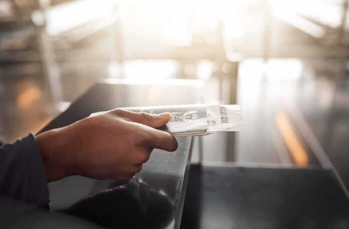 shutterstock_2482091131 Hand holding a passport and boarding pass at an airport counter