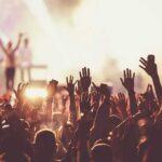 Crowd at concert with raised hands near bright stage lights