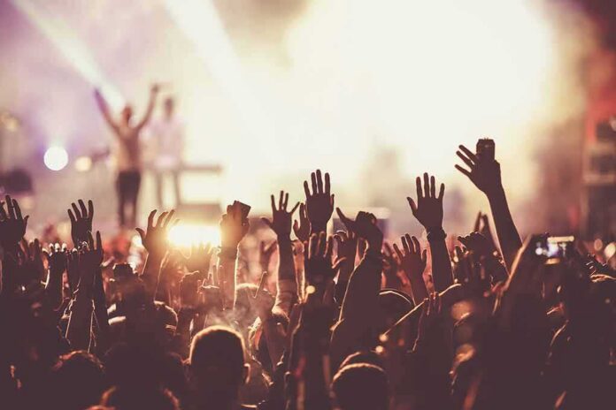 shutterstock_612941954-10 Crowd at concert with raised hands near bright stage lights