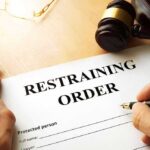 Restraining order form on a desk with hands holding a pen