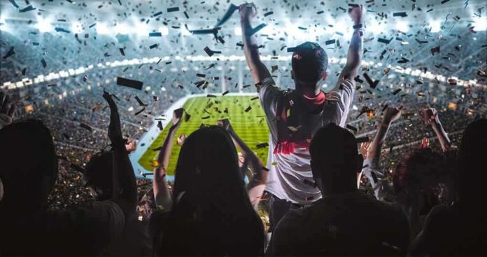 shutterstock_717281437-1 Fans celebrate in a packed stadium with confetti falling
