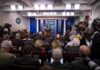 Press secretary at podium addressing reporters in briefing room