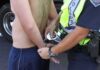 Police officer handcuffing a shirtless person roadside