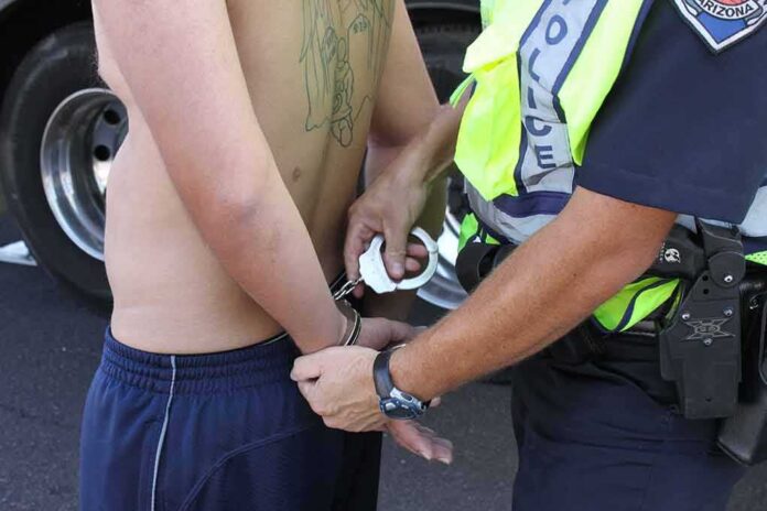 shutterstock_1421698319 Police officer handcuffing a shirtless person roadside