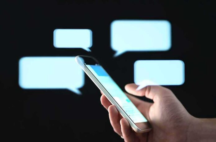 shutterstock_1452139727-1 Hand holding smartphone with chat bubbles on dark background