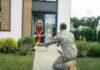 soldier kneeling to embrace daughter on home walkway
