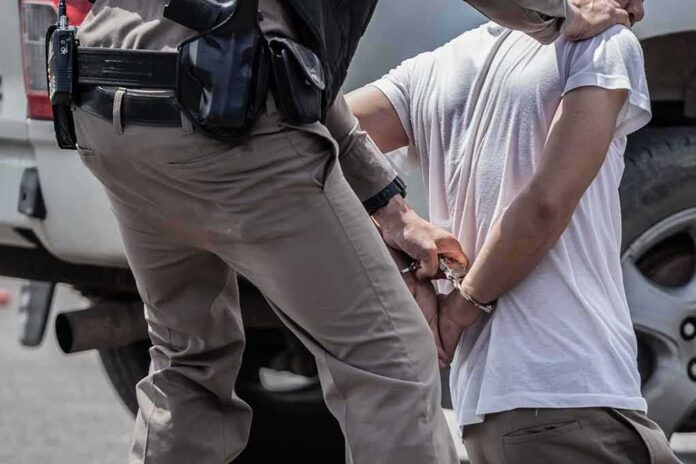 police officer handcuffing a person beside a vehicle