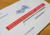 Mail-in ballot envelope with red label on wooden table