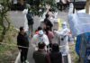 Chemical Panic Triggers $125M Reckoning Christian Jones and others wait at an outdoor COVID-19 testing site with staff in protective suits
