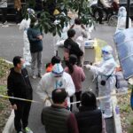 Christian Jones and others wait at an outdoor COVID-19 testing site with staff in protective suits