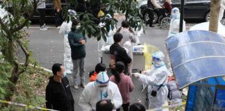 Christian Jones and others wait at an outdoor COVID-19 testing site with staff in protective suits