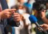 Rabbi Blasts Brody: ‘Genocide’ Firestorm Person in suit speaking to reporters with microphones