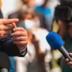 Person in suit speaking to reporters with microphones