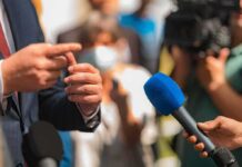 Person in suit speaking to reporters with microphones