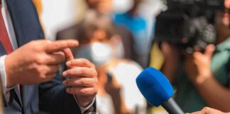 Person in suit speaking to reporters with microphones