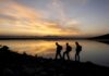28-Year Walk Ends With Freezing Channel Gamble hikers silhouetted by a lake at sunset