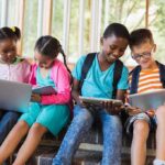 Children using laptops and tablets on school steps