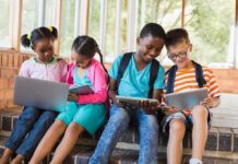 Children using laptops and tablets on school steps